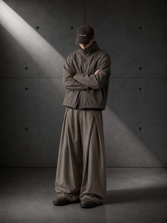 Person wearing a dark brown outfit standing against a gray concrete wall.