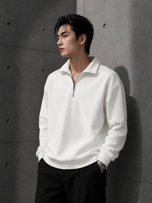 Man wearing a white half-zip sweatshirt against a gray concrete wall