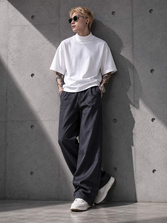 Person wearing a white turtleneck, gray pants, and white sneakers against a concrete wall.