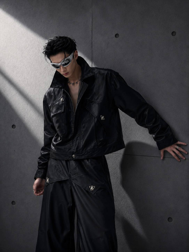 Person wearing a black outfit with reflective elements against a gray wall.