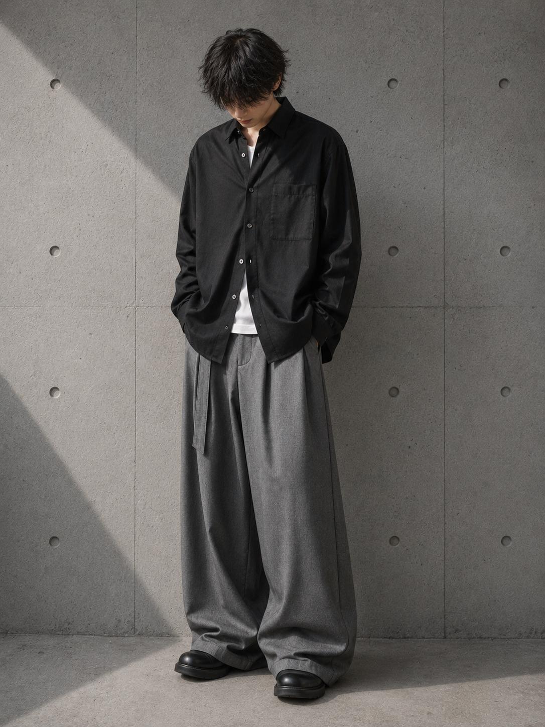 Person wearing a black jacket and gray pants against a concrete wall.