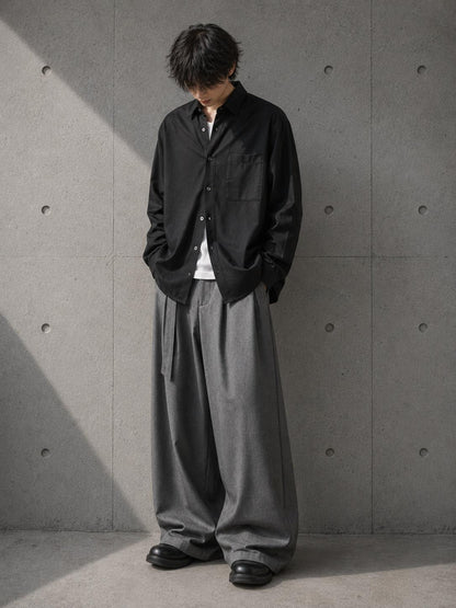 Person wearing a black jacket and gray pants against a concrete wall.