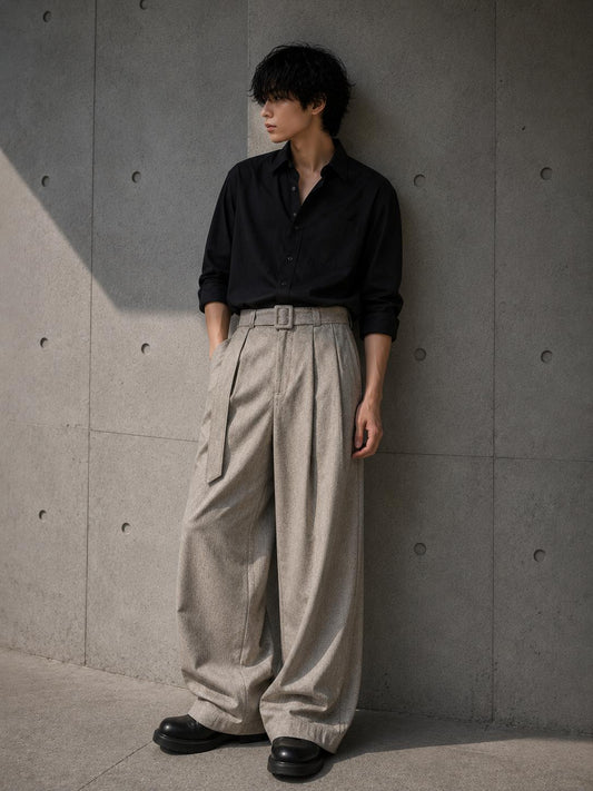 Person wearing a black shirt and beige pants against a gray concrete wall.
