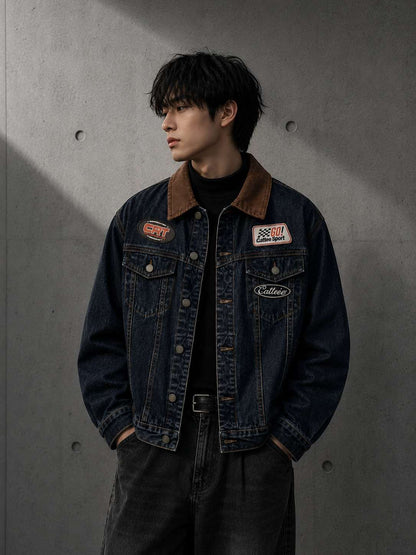 Person wearing a denim jacket with patches against a gray concrete wall