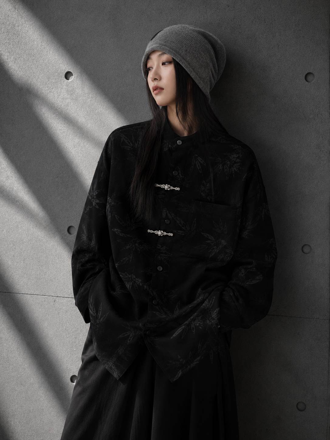 Person wearing a black jacket and gray beanie against a gray wall