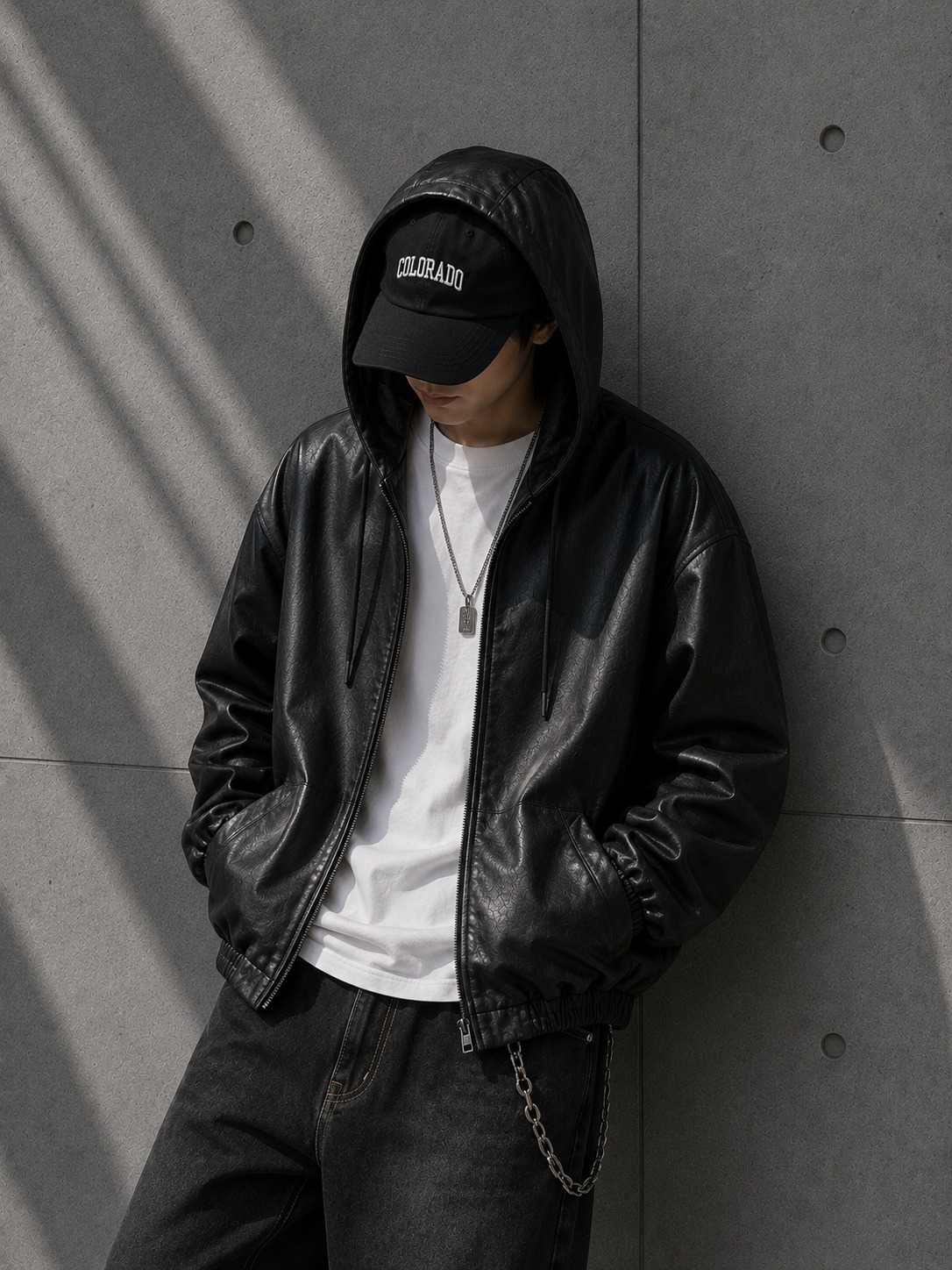 Person wearing a black leather jacket and cap against a gray wall