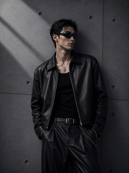 Person wearing a black leather jacket and sunglasses against a dark concrete wall.