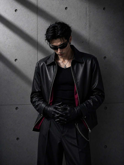 Person wearing a black leather jacket and gloves against a gray concrete wall.