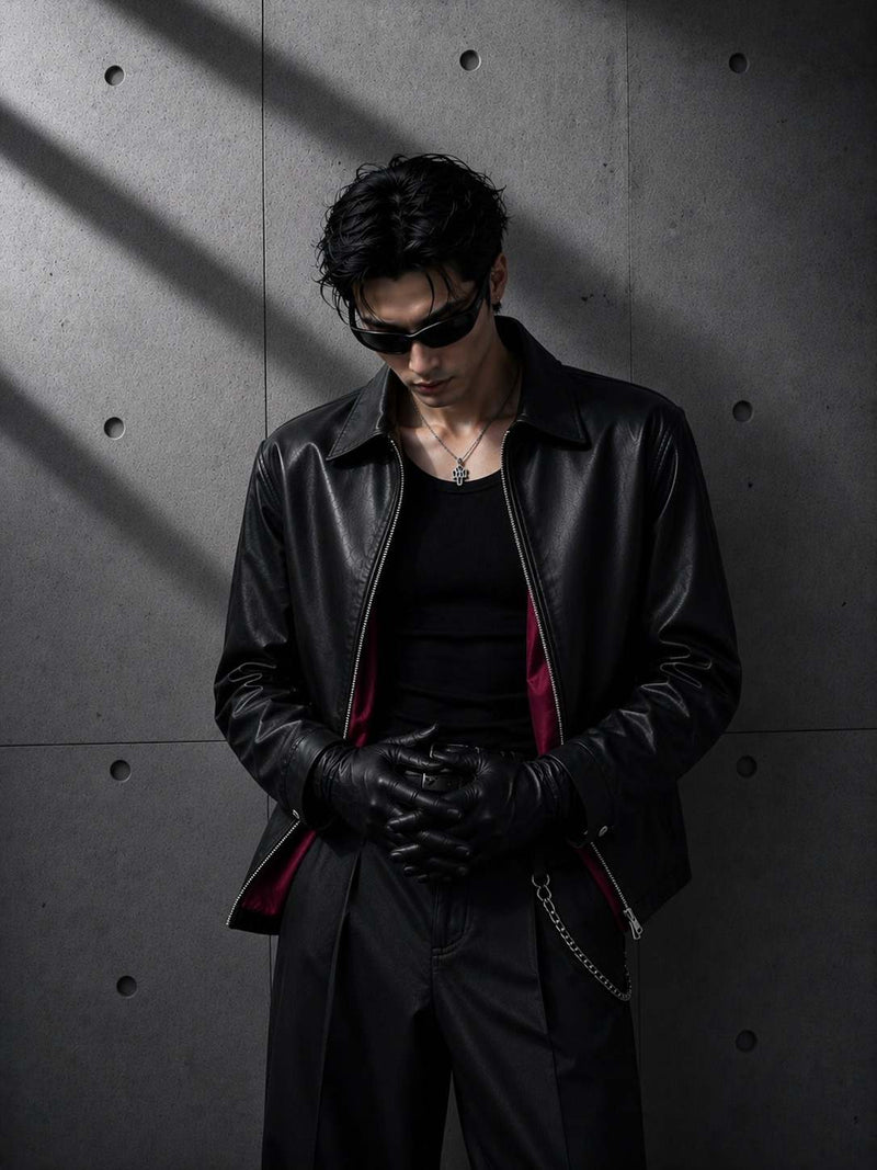 Person wearing a black leather jacket and gloves against a gray concrete wall.