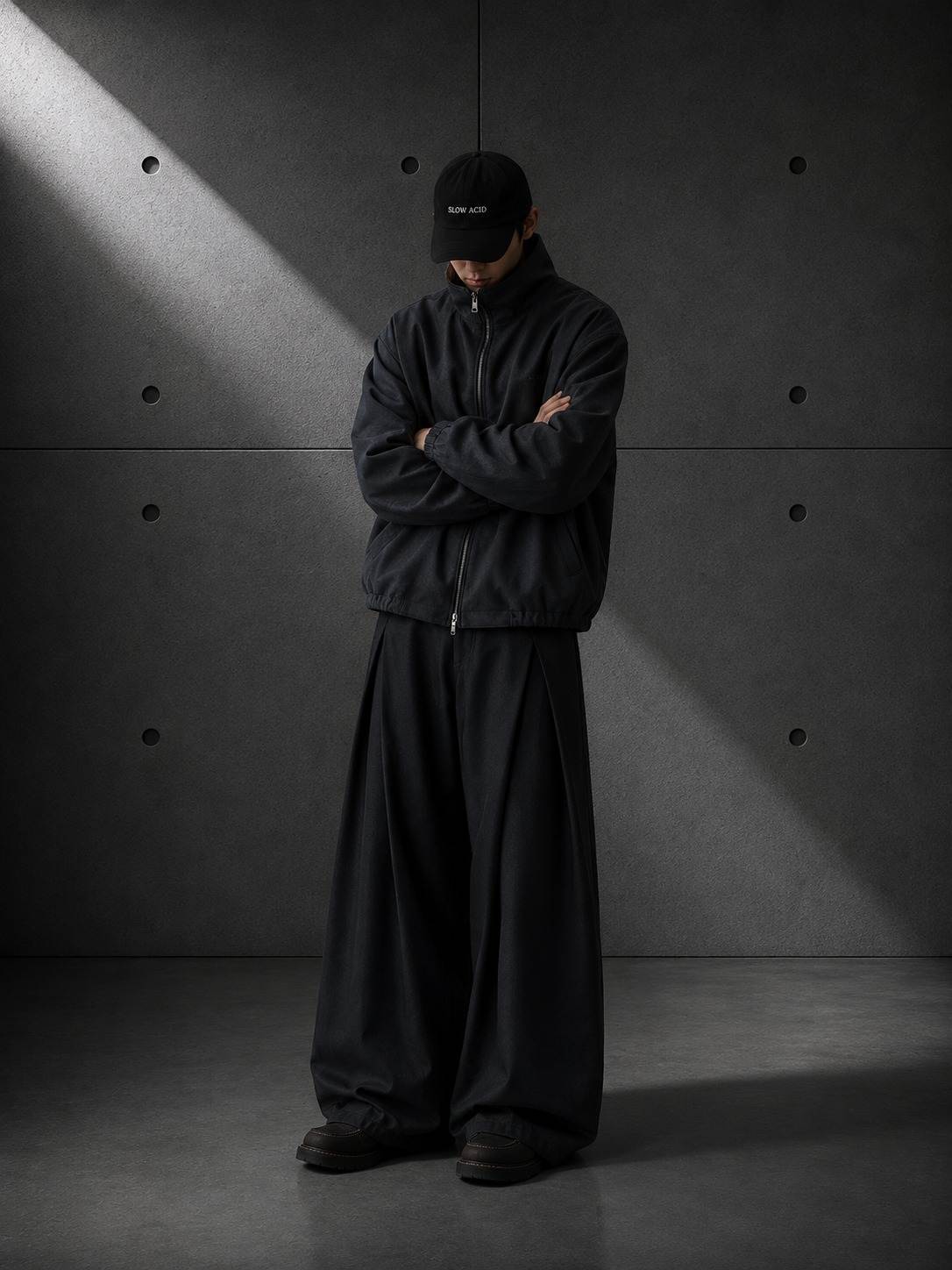 Person wearing a black outfit with a cap in a minimalistic setting