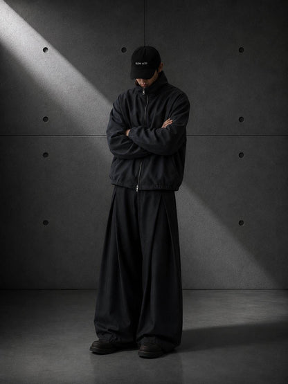 Person wearing a black outfit with a cap in a minimalistic setting