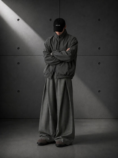 Person wearing a dark green outfit standing against a gray concrete wall.