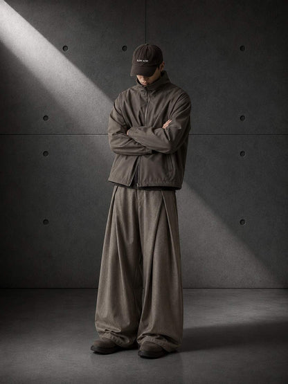 Person wearing a dark brown outfit standing against a gray concrete wall.