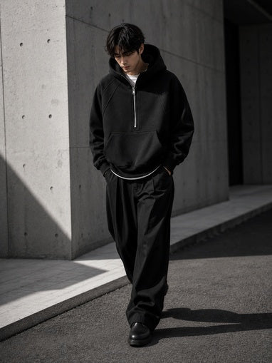 Person wearing a black tracksuit standing against a concrete wall.