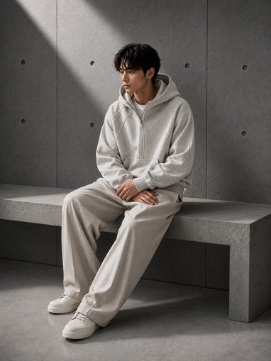 Person wearing a light gray hoodie and pants sitting on a concrete bench against a gray wall.