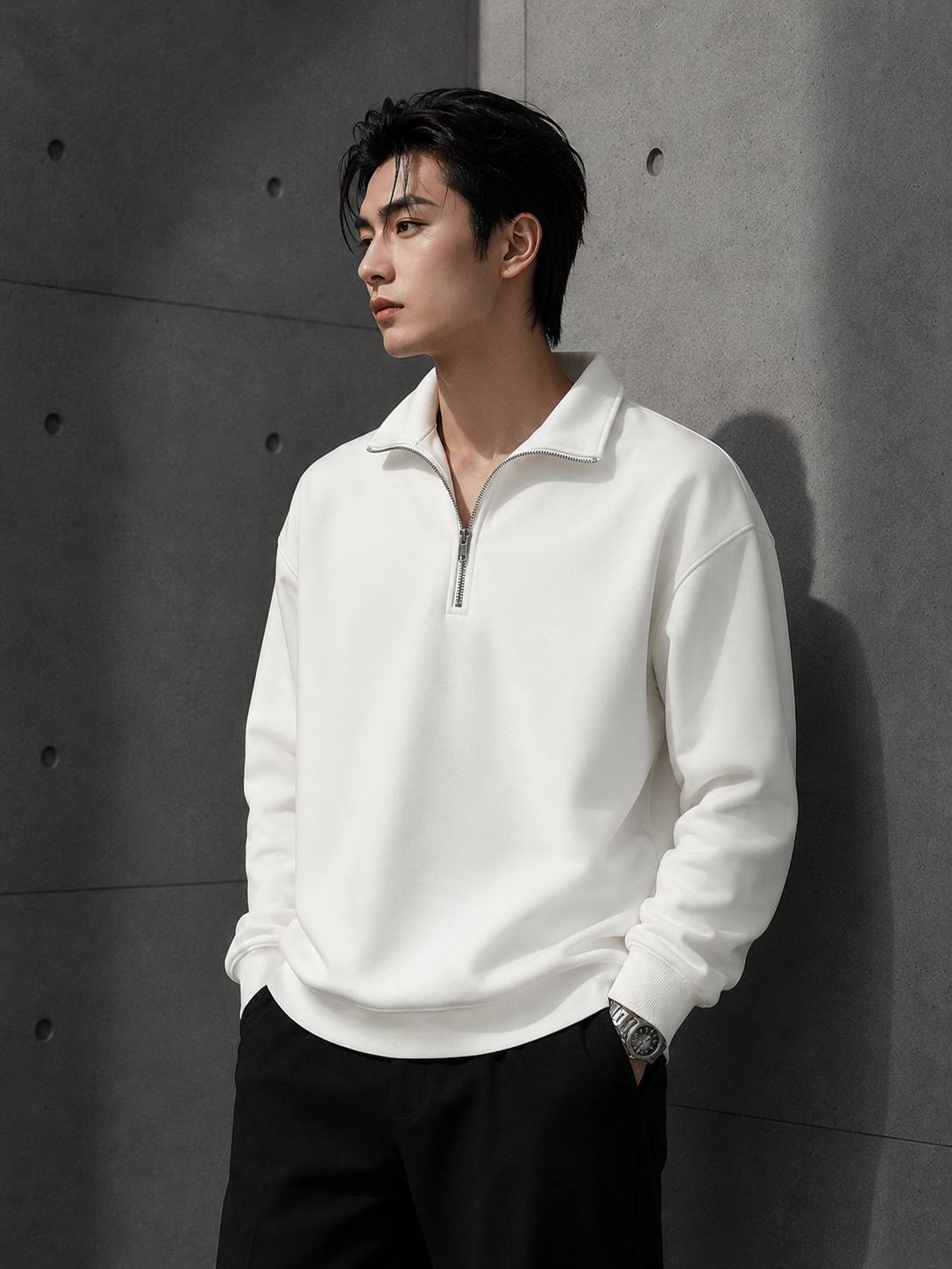 Man wearing a white half-zip sweatshirt against a gray concrete wall