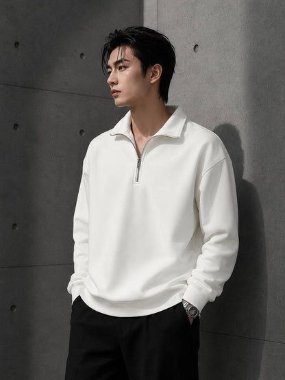 Man wearing a white half-zip sweatshirt against a gray concrete wall