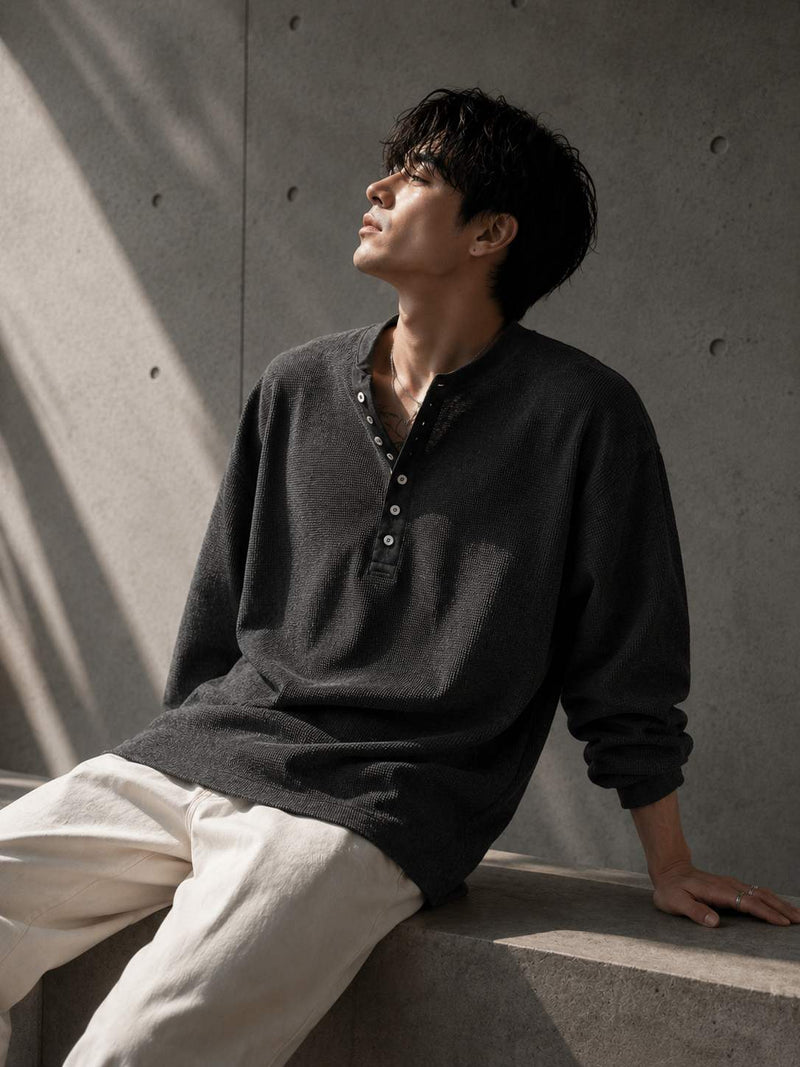 Man wearing a dark sweater and light pants against a concrete wall.