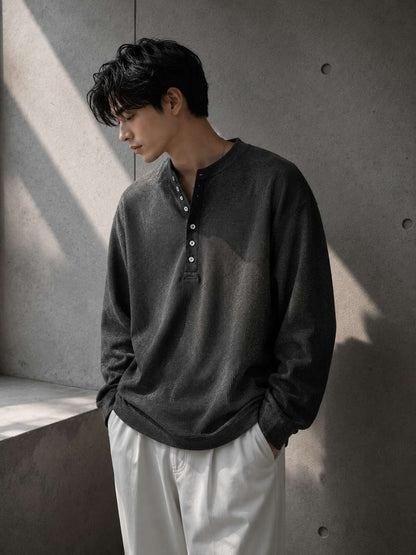 Person wearing a dark gray long-sleeve shirt with button details against a concrete wall.