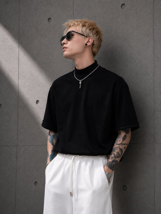 Person wearing a black t-shirt and white pants against a gray wall