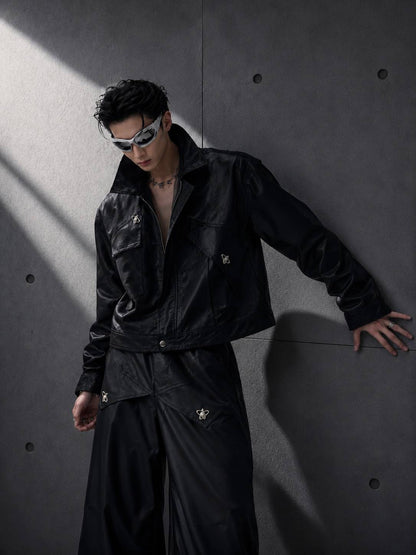 Person wearing a black outfit with reflective elements against a gray wall.