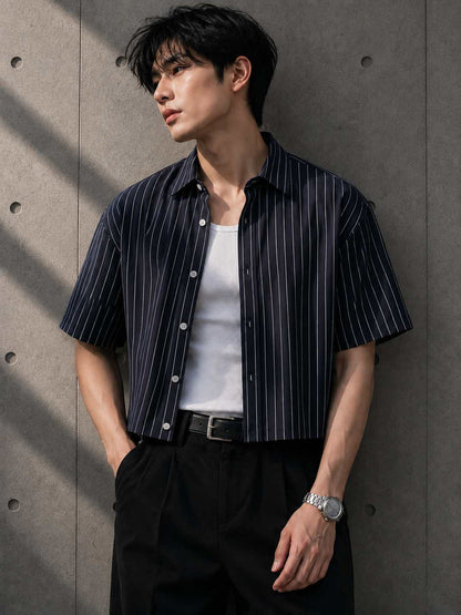 Man wearing a striped shirt over a white t-shirt against a concrete wall.