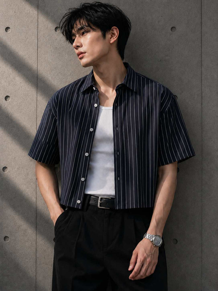 Man wearing a striped shirt over a white t-shirt against a concrete wall.