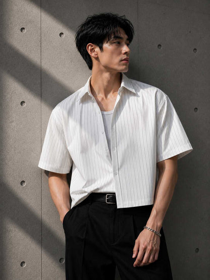 Man wearing a white striped shirt and black pants against a gray wall