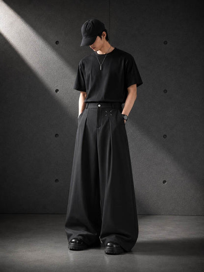 Person wearing a black outfit with wide-leg pants against a dark background