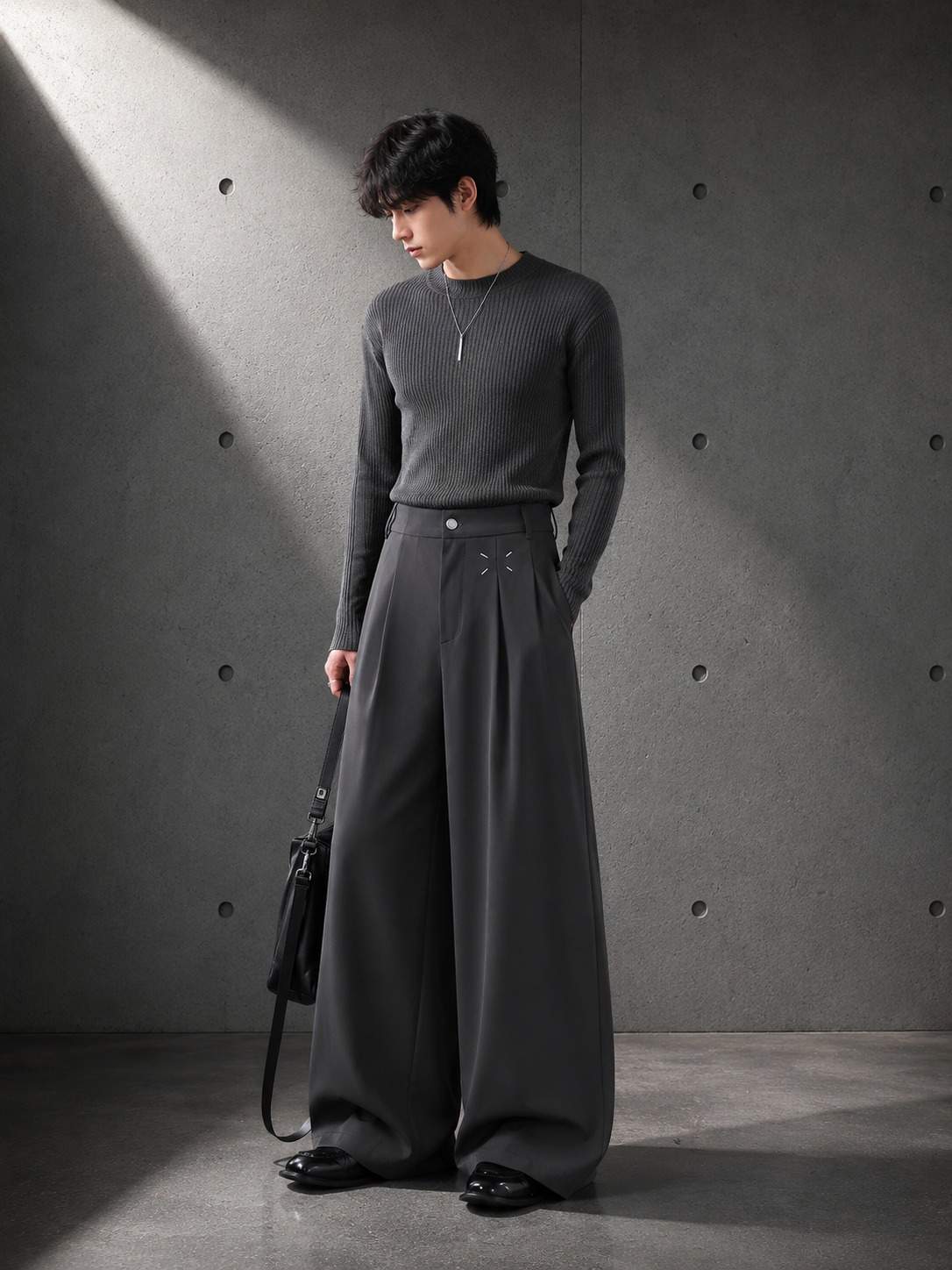 Person wearing gray Pleat Wide Leg Trousers against a dark background — LARÉN
