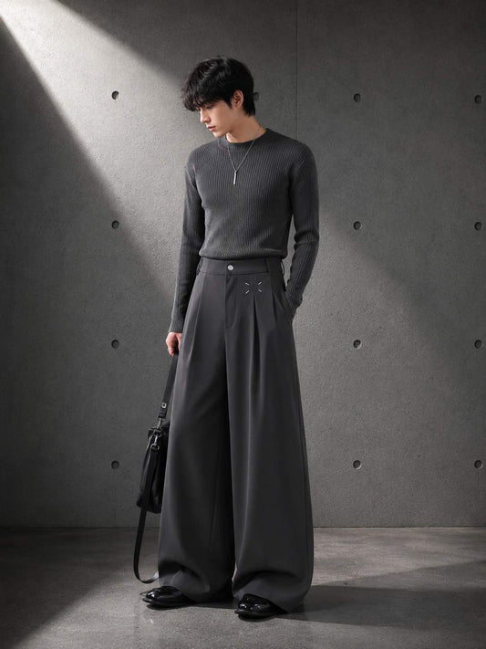 Person wearing gray Pleat Wide Leg Trousers against a dark background — LARÉN