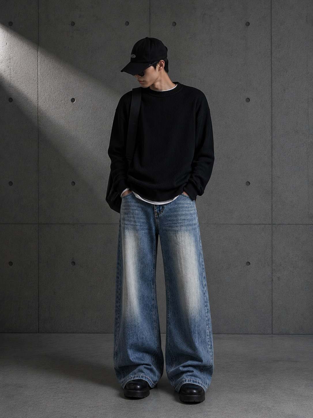 Person wearing a black sweater and blue jeans against a gray concrete wall.