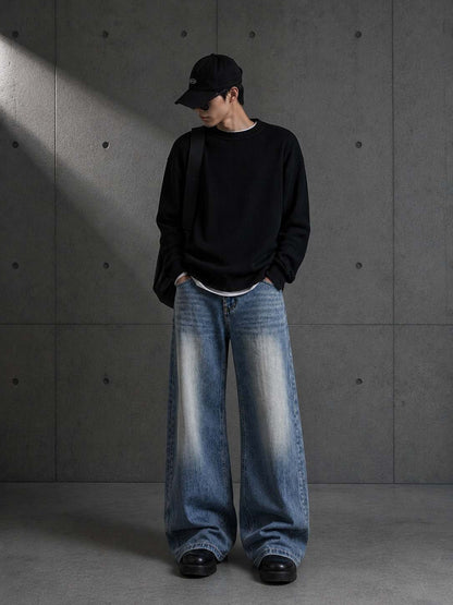 Person wearing a black sweater and blue jeans against a gray concrete wall.