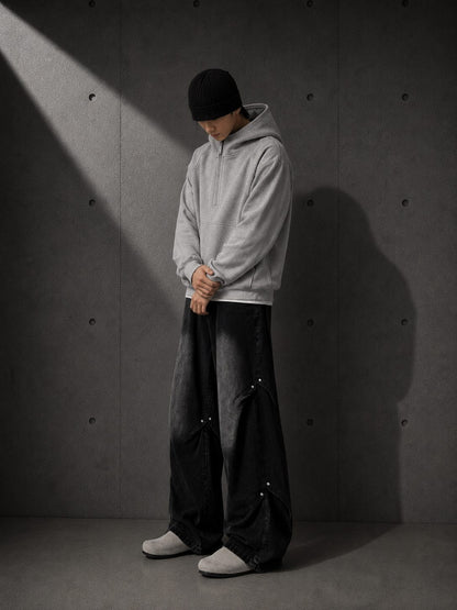 Person wearing a gray hoodie and dark pants against a textured gray wall.