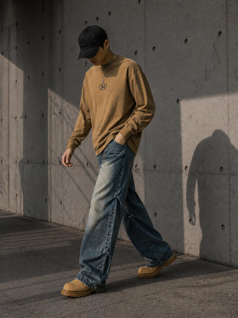 Person wearing a beige sweater, blue jeans, and brown shoes against a concrete wall.