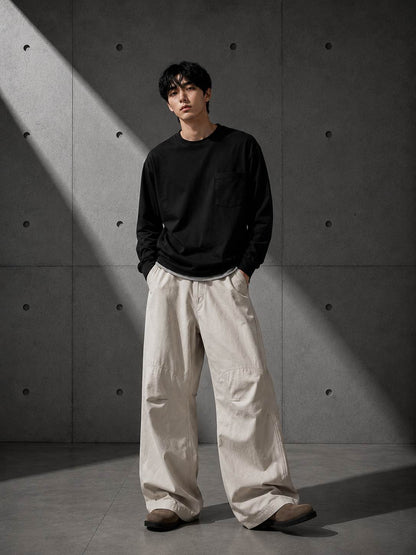 Person wearing a black sweater and beige pants against a textured gray wall.