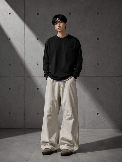 Person wearing a black sweater and beige pants standing against a concrete wall.