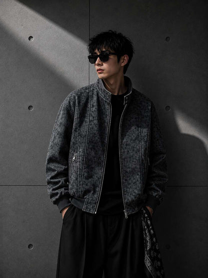 Man wearing a dark denim jacket and sunglasses against a gray concrete wall.