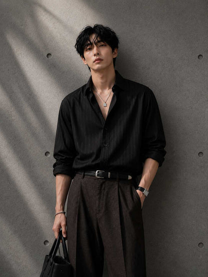 Man wearing a black shirt and dark pants against a gray wall