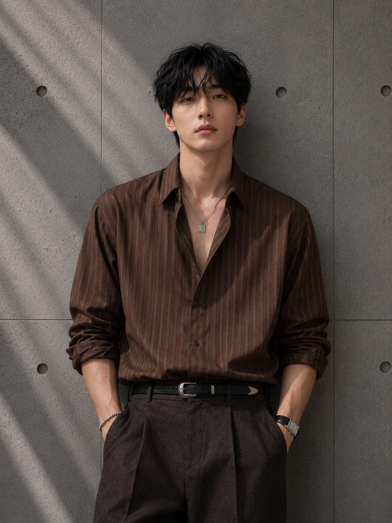 Man wearing a brown striped shirt and dark pants against a gray concrete wall.