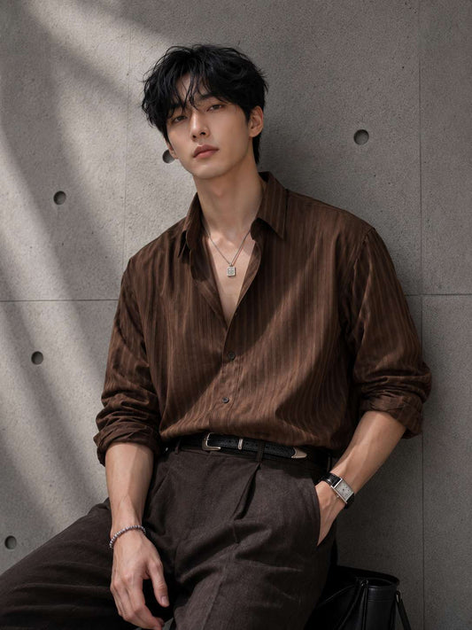 Man wearing a brown shirt and pants against a gray concrete wall.