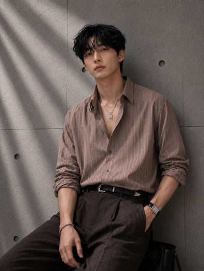 Man in a brown stitch stripe shirt seated against a gray concrete wall