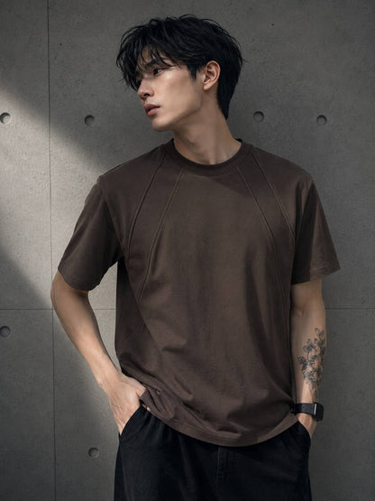 Man wearing a brown t-shirt against a gray concrete wall