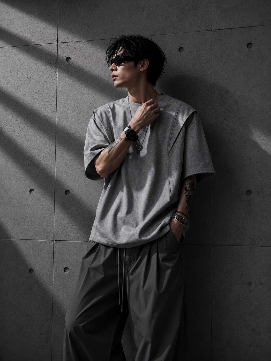 Person wearing a gray oversized t-shirt and dark pants against a textured wall.