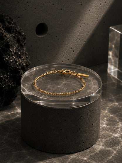 Gold bracelet on a clear circular stand with a dark textured background