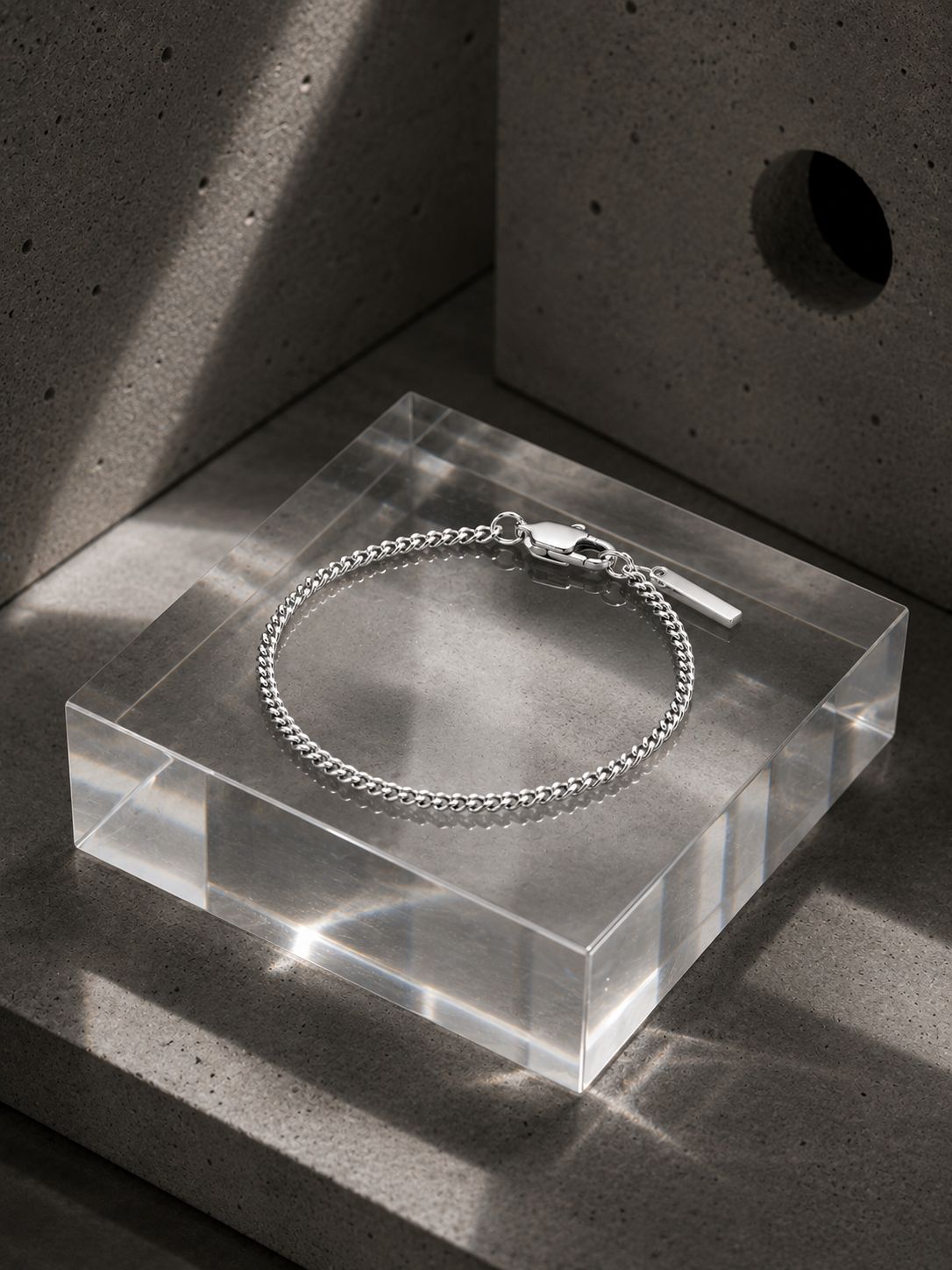 Silver bracelet on a clear acrylic block with a concrete background