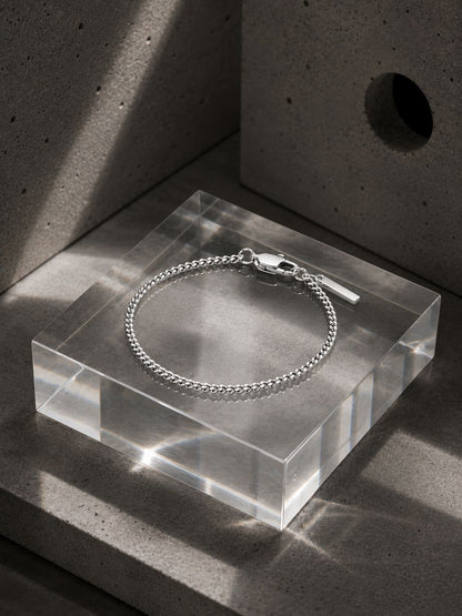 Silver bracelet on a clear acrylic block with a concrete background