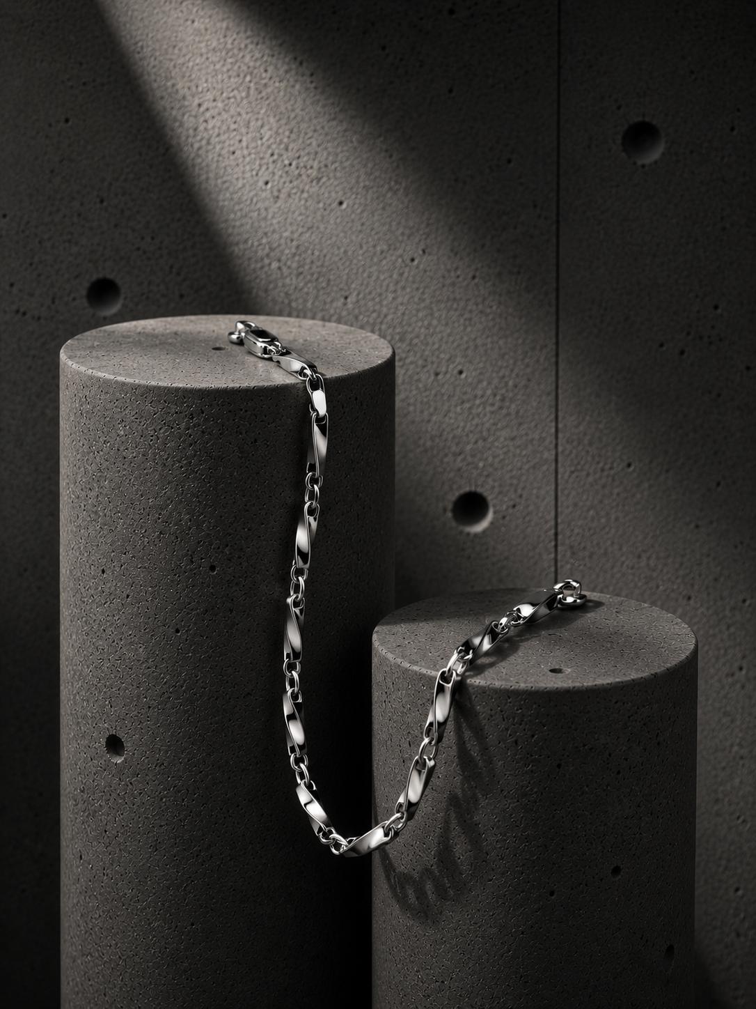 Silver chain bracelet on a cylindrical concrete block against a dark textured background