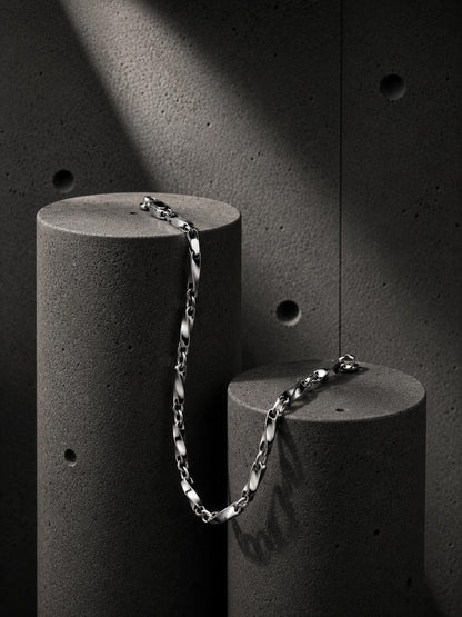 Silver chain bracelet on a cylindrical concrete block against a dark textured background