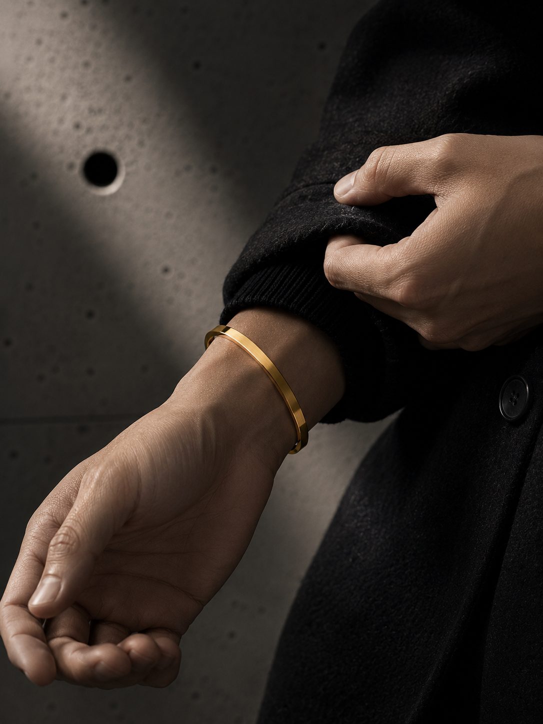 Close-up of a person's wrist wearing a gold bracelet against a dark background